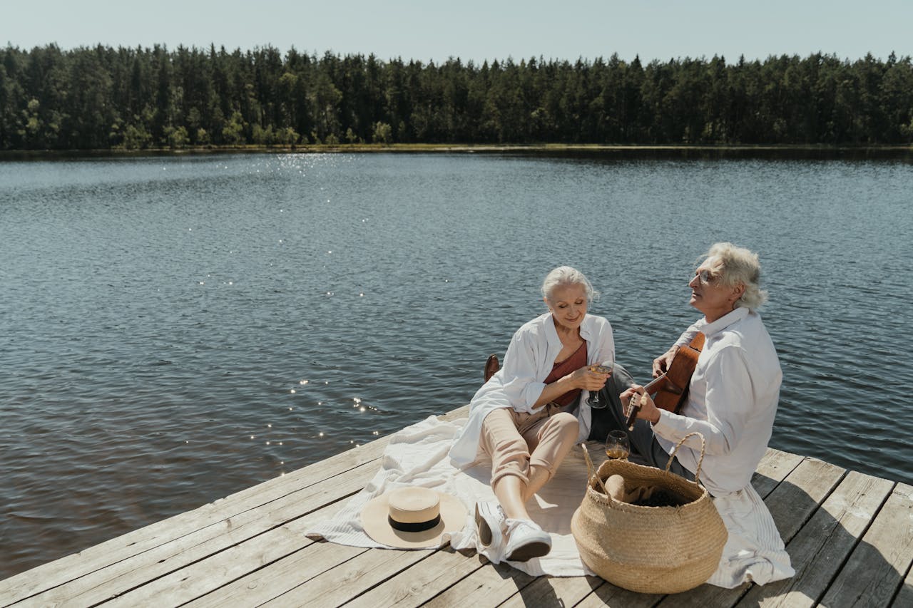 Home Elderly couple relaxing by a lake, enjoying music and nature, symbolizing peaceful retirement days.